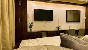 Ett hotellrum med en stor säng, en platt-TV som är monterad på väggen, ett skrivbord med en stol och en spegel ovanför skrivbordet.