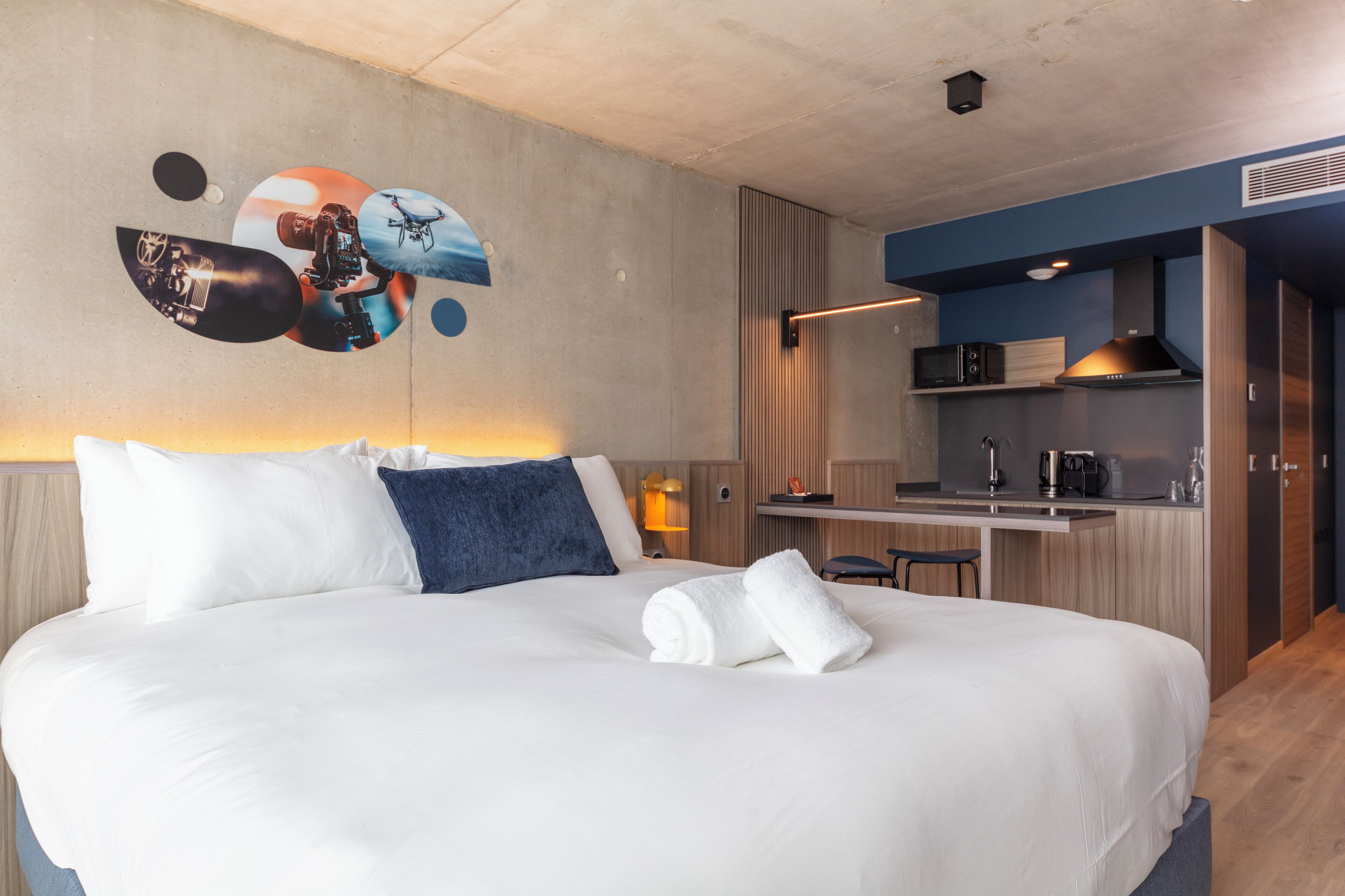 Une chambre d’hôtel moderne avec un grand lit, une petite kitchenette et une œuvre d’art accrochée au mur.