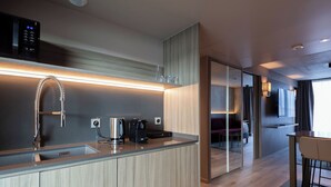 Una cocina moderna con cafetera integrada, hervidor y microondas. Hay un panel de vidrio que separa la cocina del comedor.