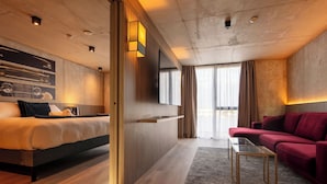 Una habitación de hotel moderna con una cama, un sofá rojo, un televisor y un ventanal con cortinas.