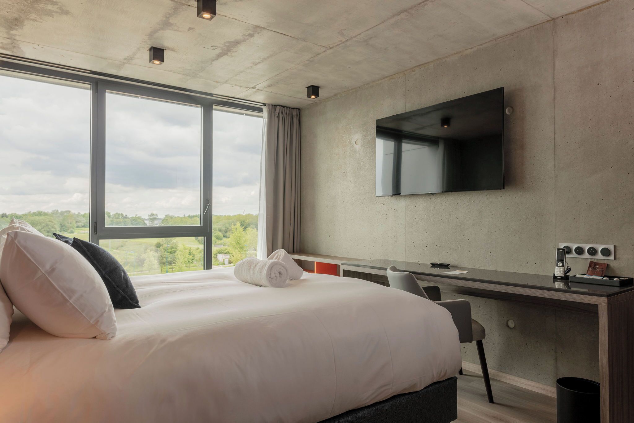 A modern hotel room with a large bed, a desk, and a TV mounted on the wall.