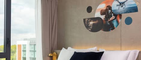 A hotel room with a bed, pillows, a window, and a wall with a circular design.