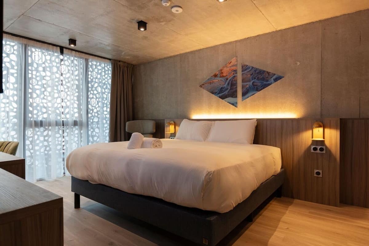 A modern bedroom with a large bed, wooden headboard, and a decorative wall piece.
