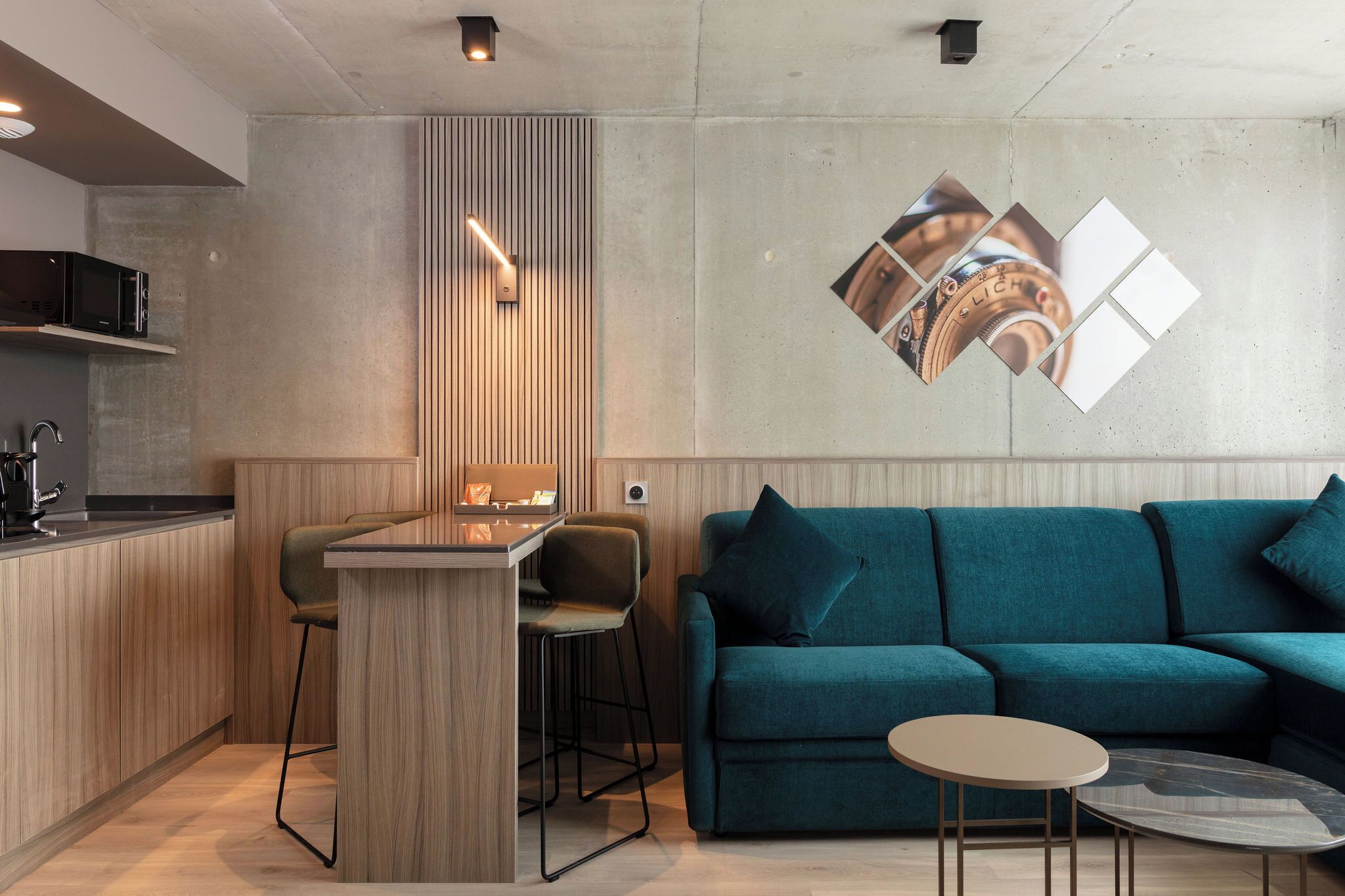 Une cuisine moderne avec un îlot central en bois, des tabourets de bar et un canapé turquoise agrémenté d’une petite table ronde.