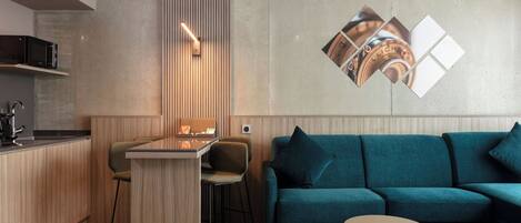 A modern kitchen with a wooden island, bar stools, and a teal sofa with a small round table.