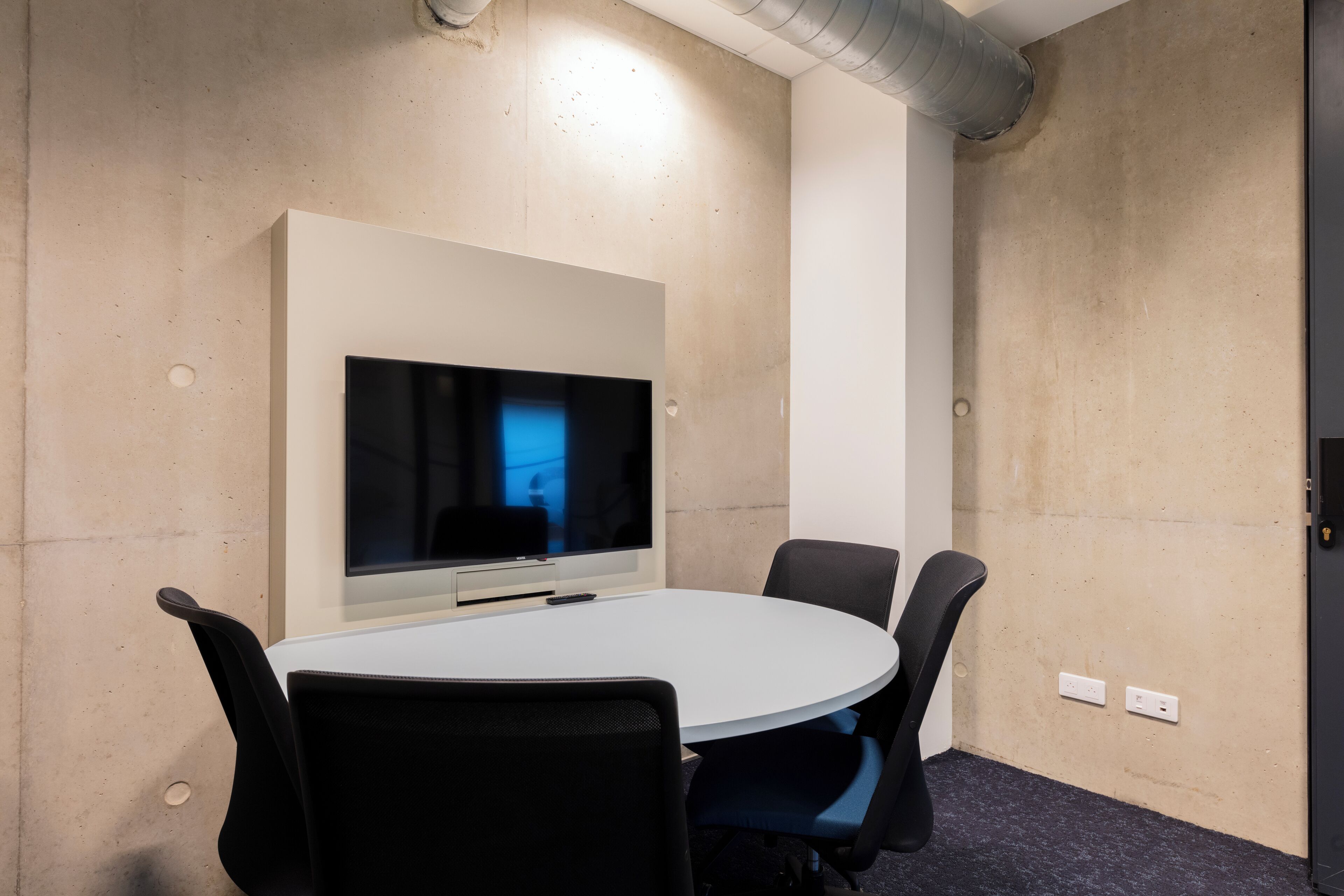 Une salle de conférence équipée d’un grand téléviseur à écran plat, d’une table blanche et de chaises noires.