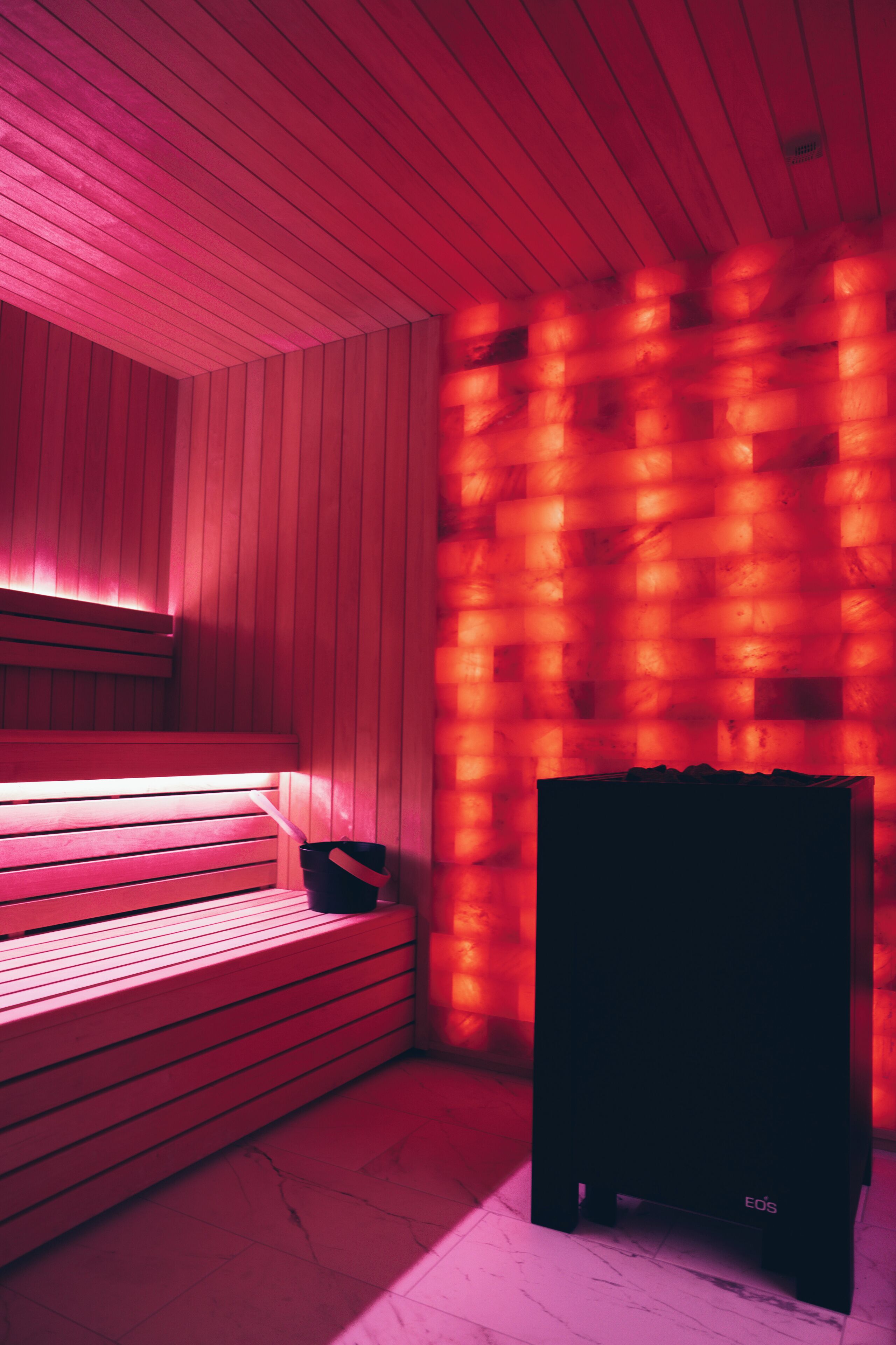 A sauna room with wooden benches and a black heater labeled "EOS".