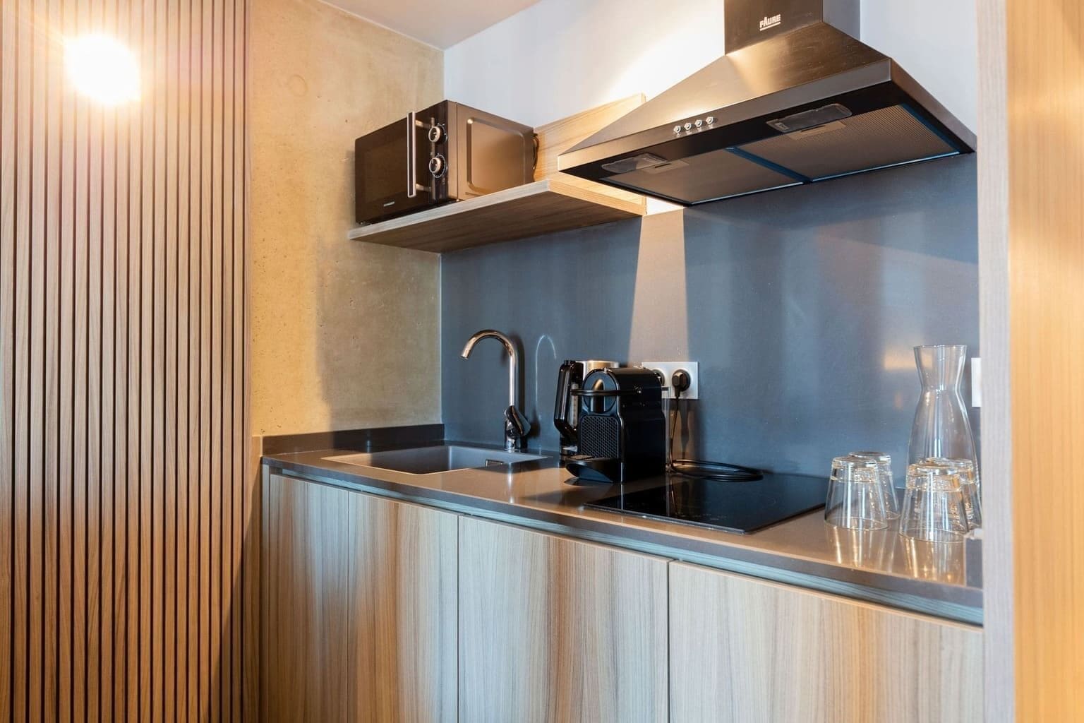 A modern kitchen with a built-in microwave, a stainless steel range hood, and a glass countertop.
