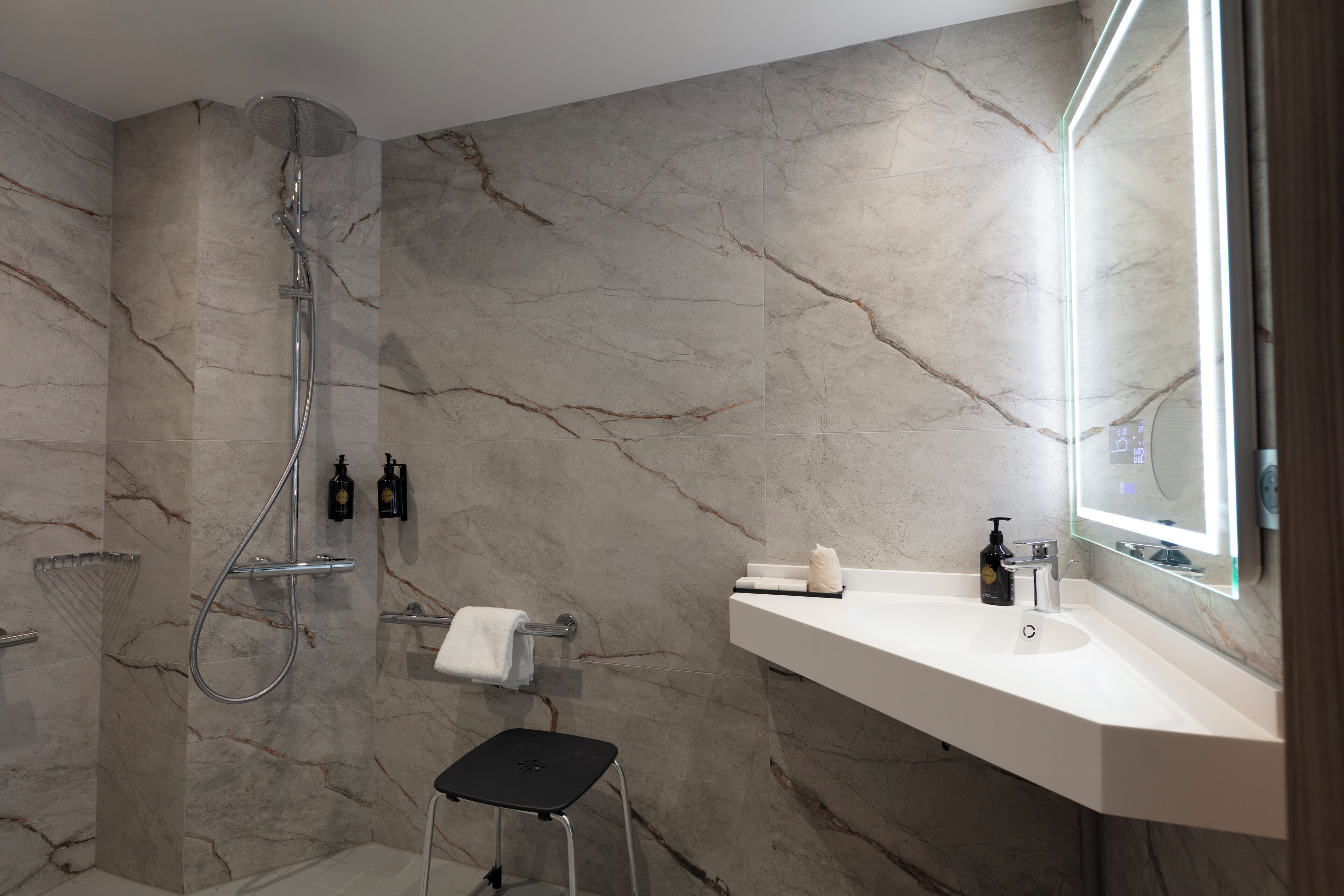Une salle de bain moderne avec un mur en marbre, une douche, un lavabo et un miroir.
