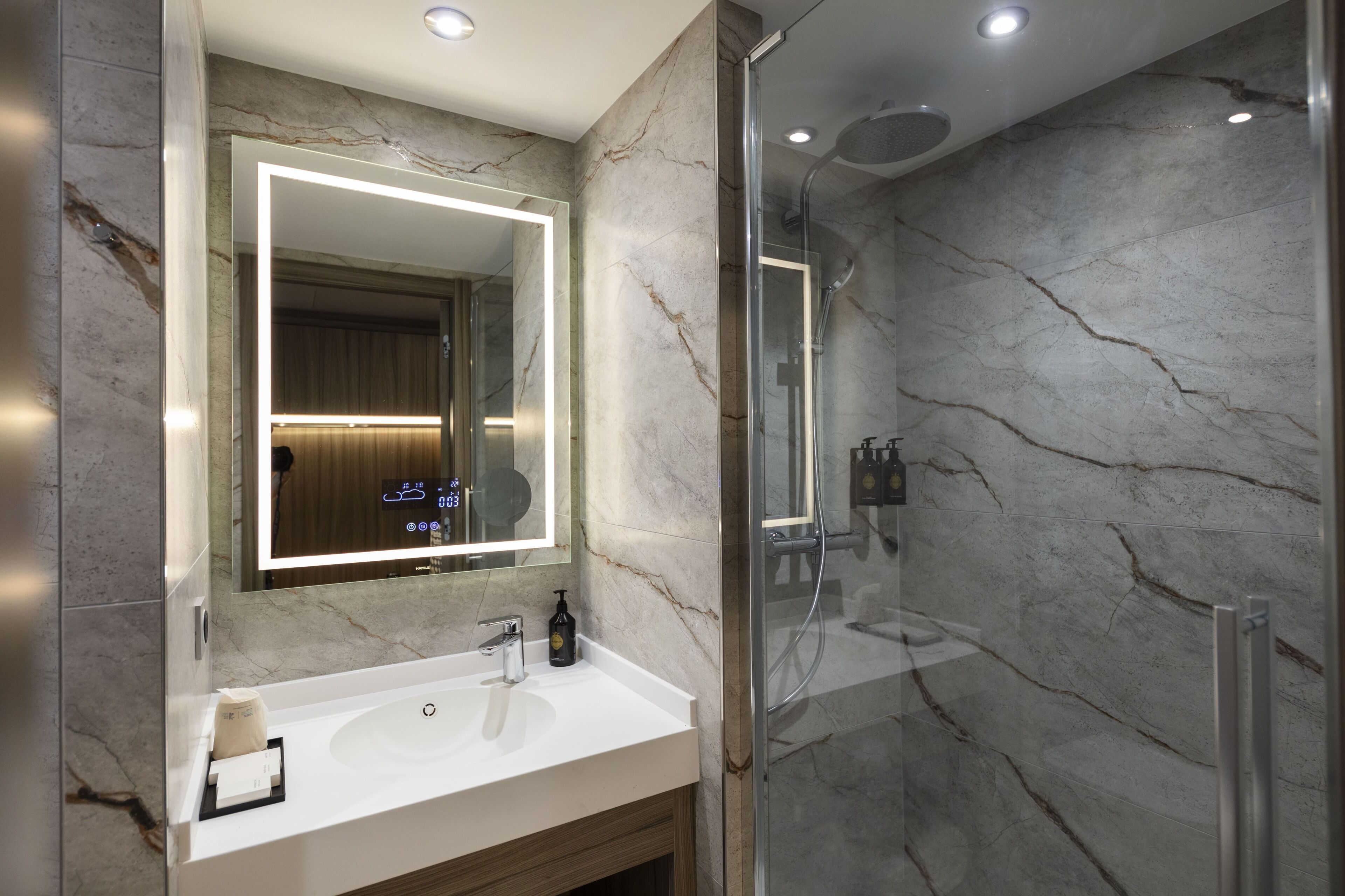 Un baño moderno con lavamanos de mármol, un espejo grande y una ducha con mampara de vidrio.