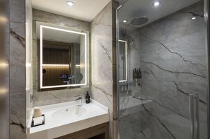 Un baño moderno con lavamanos de mármol, un espejo grande y una ducha con mampara de vidrio.