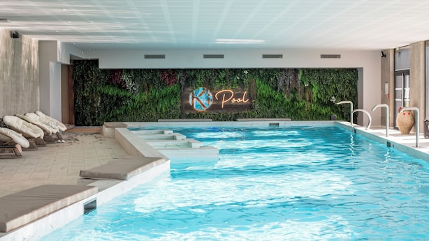Una piscina interior con un letrero de neón que dice "Pool" y una pared cubierta de follaje verde.