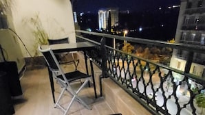 A balcony with a glass table and chairs, a railing, and a view of the cityscape at night. - LView Zeus Temple (Athens)