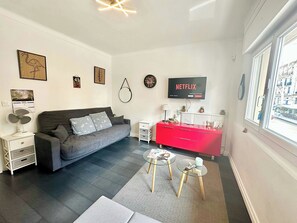 Una sala de estar moderna con un sofá gris, un mueble de almacenamiento rojo, una mesa de centro de vidrio y un televisor que muestra 'NETFLIX'.