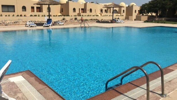 A swimming pool with lounge chairs and umbrellas, surrounded by buildings with dome-shaped roofs. - Sea View Duplex Villa Hurghada  (Red Sea Governorate)