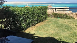 A view of a grassy area with a table and chairs, a hedge, and a distant view of the sea and a building. - Sea View Duplex Villa Hurghada  (Red Sea Governorate)