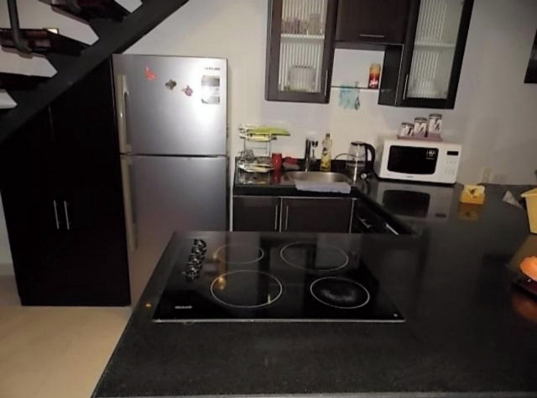 Uma cozinha com bancada preta, fogão, geladeira e micro-ondas.