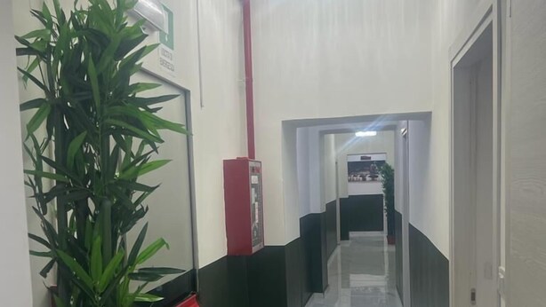 A hallway with a marble floor, a potted plant, a red pillar, and a chandelier. - Hotel Roma Palace (Rome)