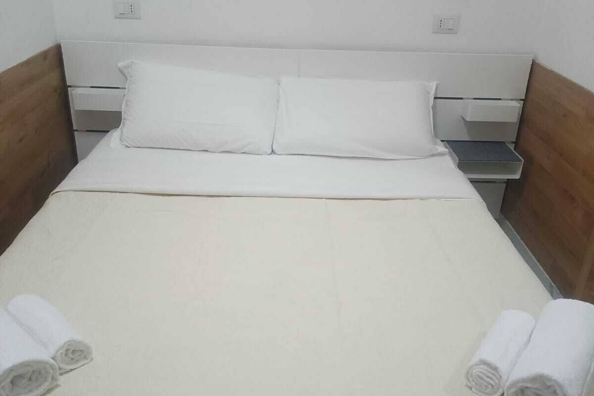 A single bed with a wooden headboard, white bedding, and two rolled towels on the side.