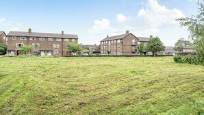 A residential area with brick houses, a grassy field, and trees.