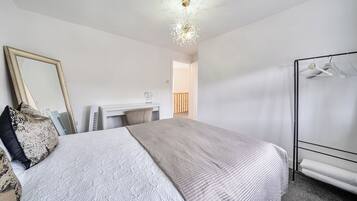 A bedroom with a bed, a dresser, a mirror, a hanging clothes rack, and a ceiling light fixture.
