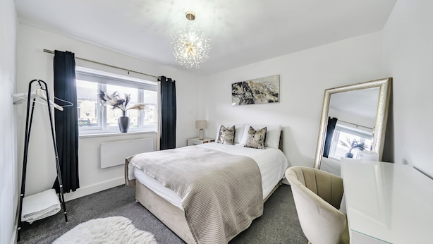 A bedroom with a bed, bedside tables, a dresser, a mirror, a window with curtains, and a hanging light fixture.
