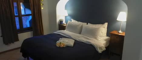 A neatly made bed with white linens, two bedside lamps, and a small table with a lamp and a plant.