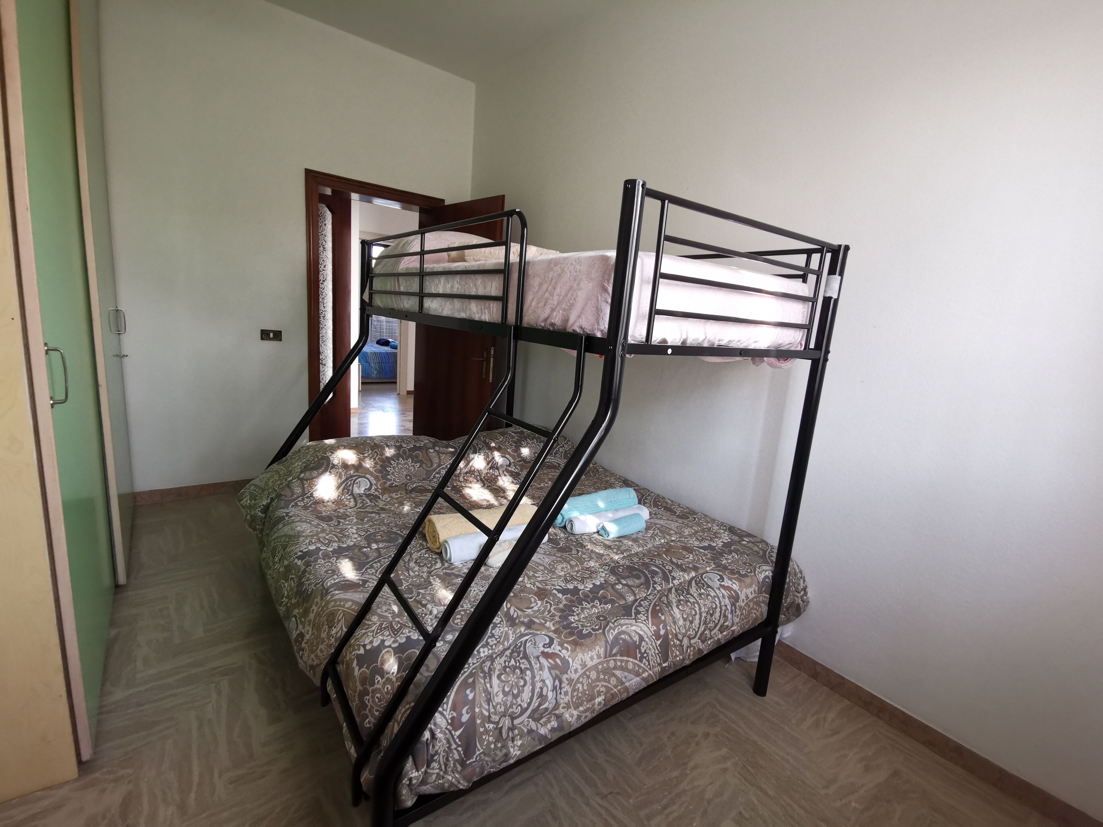 Een stapelbed met een gestreept matras, een houten deur en een betegelde vloer.