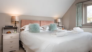 Una cama bien hecha con almohadas mullidas, una mesita de noche con lámpara y una ventana con cortinas.