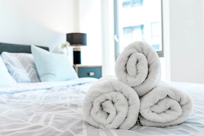 A neatly made bed with white linens and rolled towels in the foreground. - The Oxx - Canary Wharf (London)