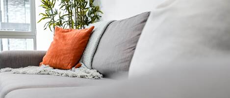 En grå soffa med en vit pläd och en orange kudde.