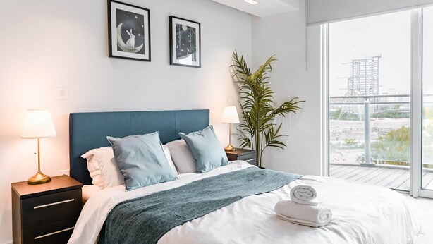 A modern bedroom with a large bed, two bedside tables, a nightstand, a potted plant, and framed artwork on the wall.