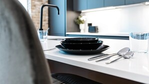 Une cuisine moderne avec un plan de travail blanc, des assiettes noires et des couverts en argent.