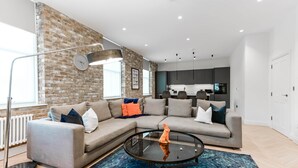 Un salon moderne avec un canapé d’angle, une table basse en verre et un mur décoratif en briques.