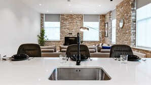Una zona d'esmorzar moderna amb taula blanca, plats negres i un rentaplat de stainless steel.