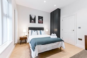 Un dormitorio moderno con una cama, dos lámparas de pared, una puerta y dos cuadros enmarcados.