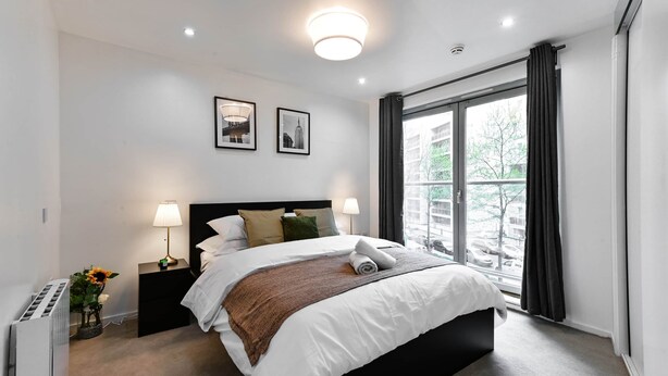 Quarto de hotel moderno com uma cama grande, duas luminárias de cabeceira, uma janela com cortinas e um radiador.