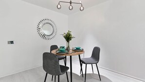 Uma área de refeições com uma mesa redonda, quatro cadeiras cinzas, um vaso com flores e um lustre moderno.