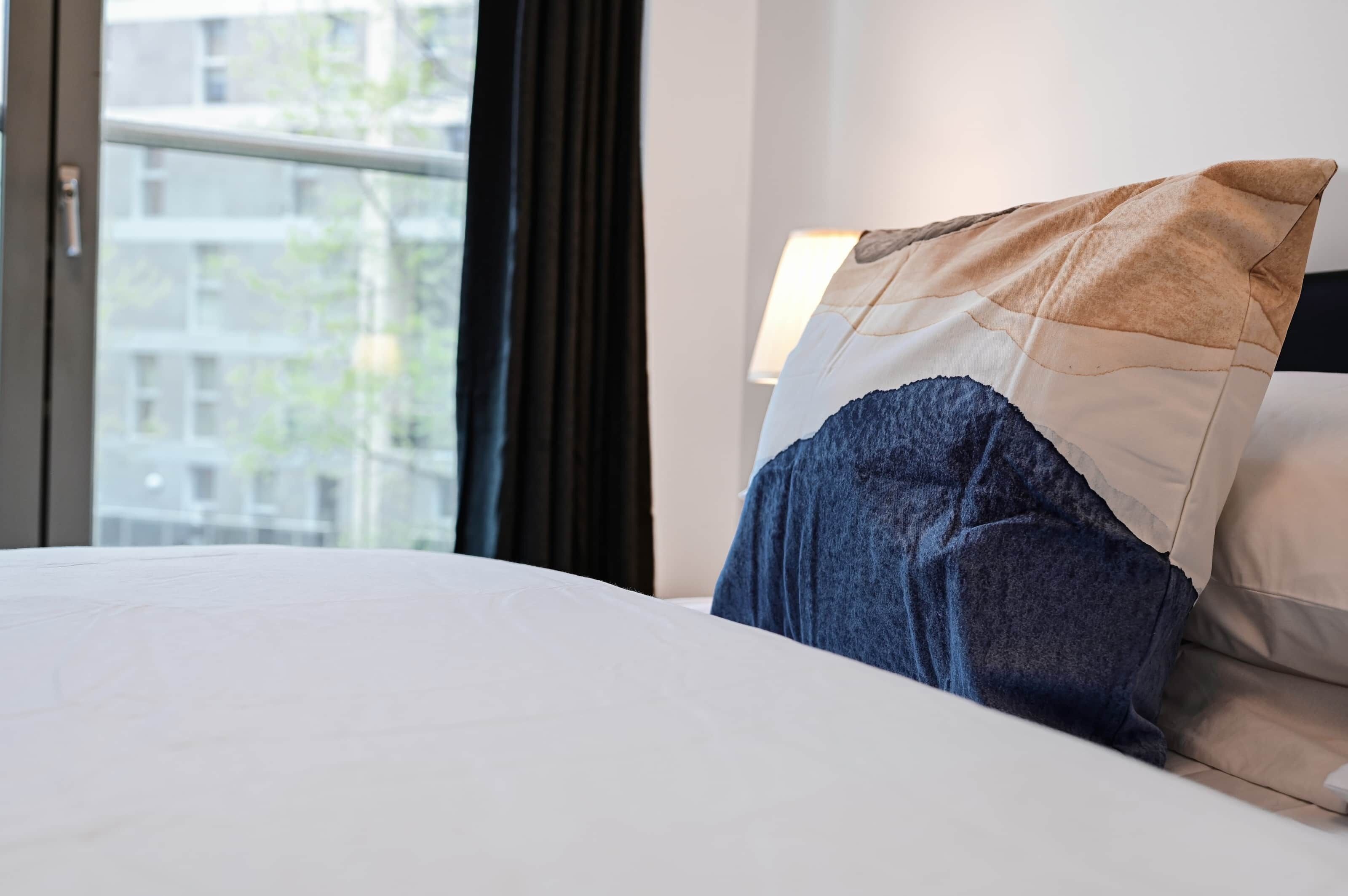 A hotel room with a bed, a window with curtains, and a view of buildings outside.
