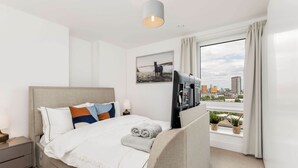 A modern hotel room with a bed, a TV, a window with curtains, and a city view. - The Ferre - Canary Wharf (London)