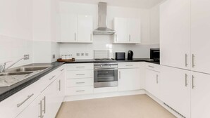A modern kitchen with white cabinets, stainless steel appliances, and a black countertop. - The Ferre - Canary Wharf (London)