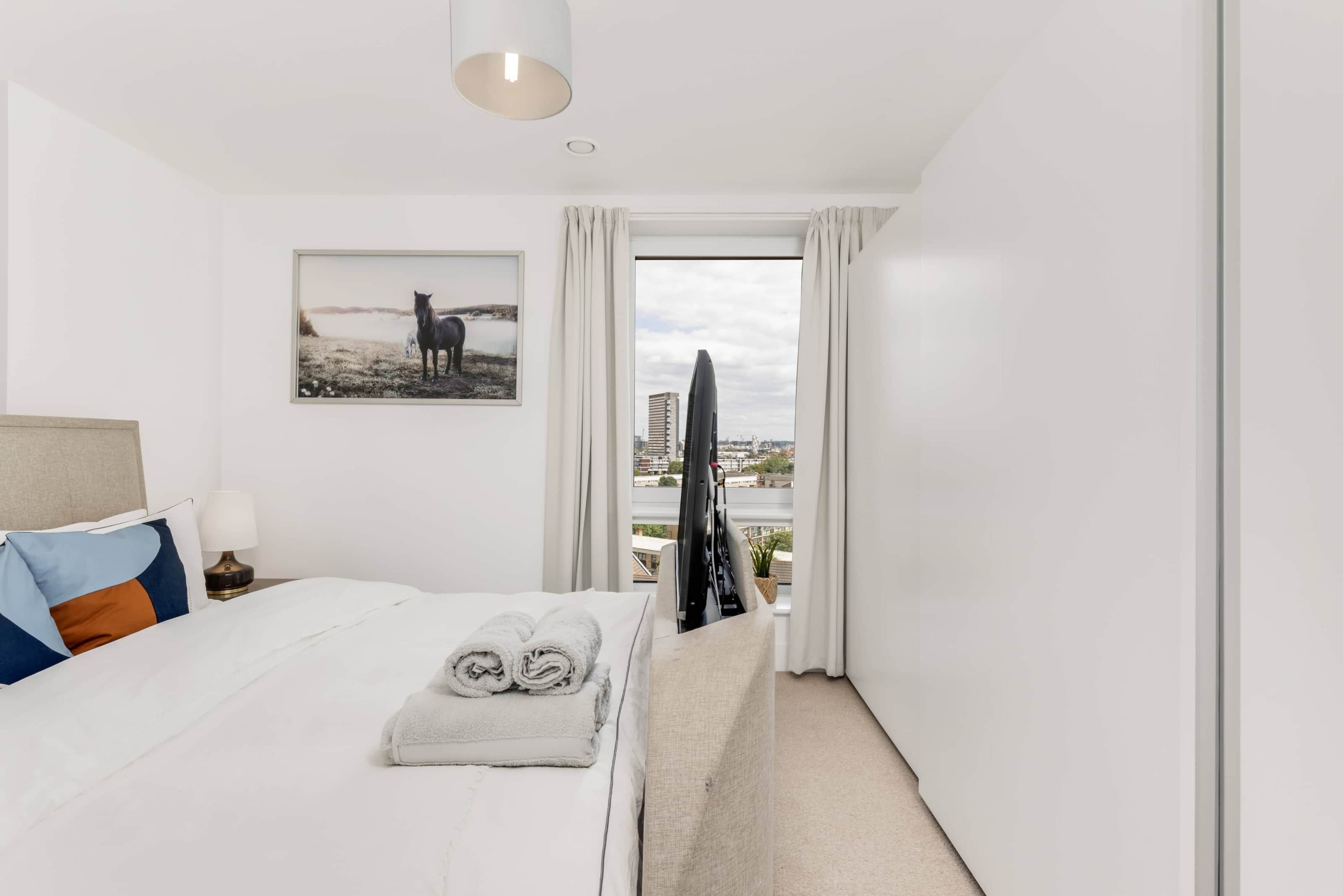 A hotel room with a bed, a TV, a window with curtains, and a painting on the wall.