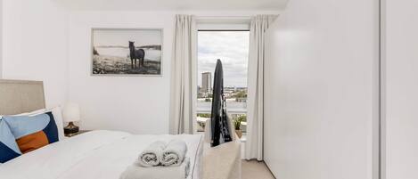 A hotel room with a bed, a TV, a window with curtains, and a painting on the wall.