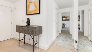 A hallway with a modern console table, a framed abstract painting, and a rug leading to a room. - The Ferre - Canary Wharf (London)
