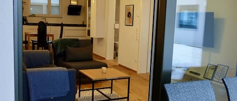 Una sala de estar moderna con un sofá, una mesa de centro y un sillón. Cuenta con una zona de cocina con armarios y una ventana.