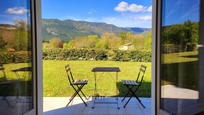 Un pati amb dues taules i cadires, i vista a un paisatge de muntanyes a través de grans portes de vidre.