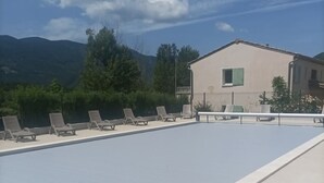 Una piscina amb gandules, un edifici amb un balcó i muntanyes al fons.
