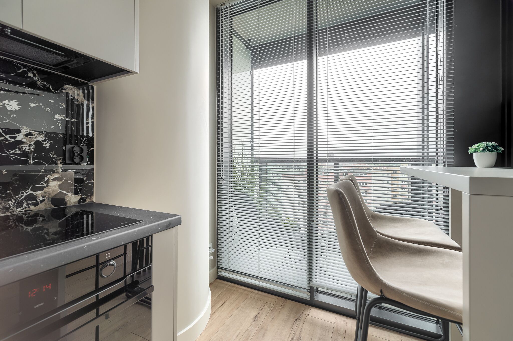A modern kitchen with a black countertop, a built-in oven, and a window with blinds.