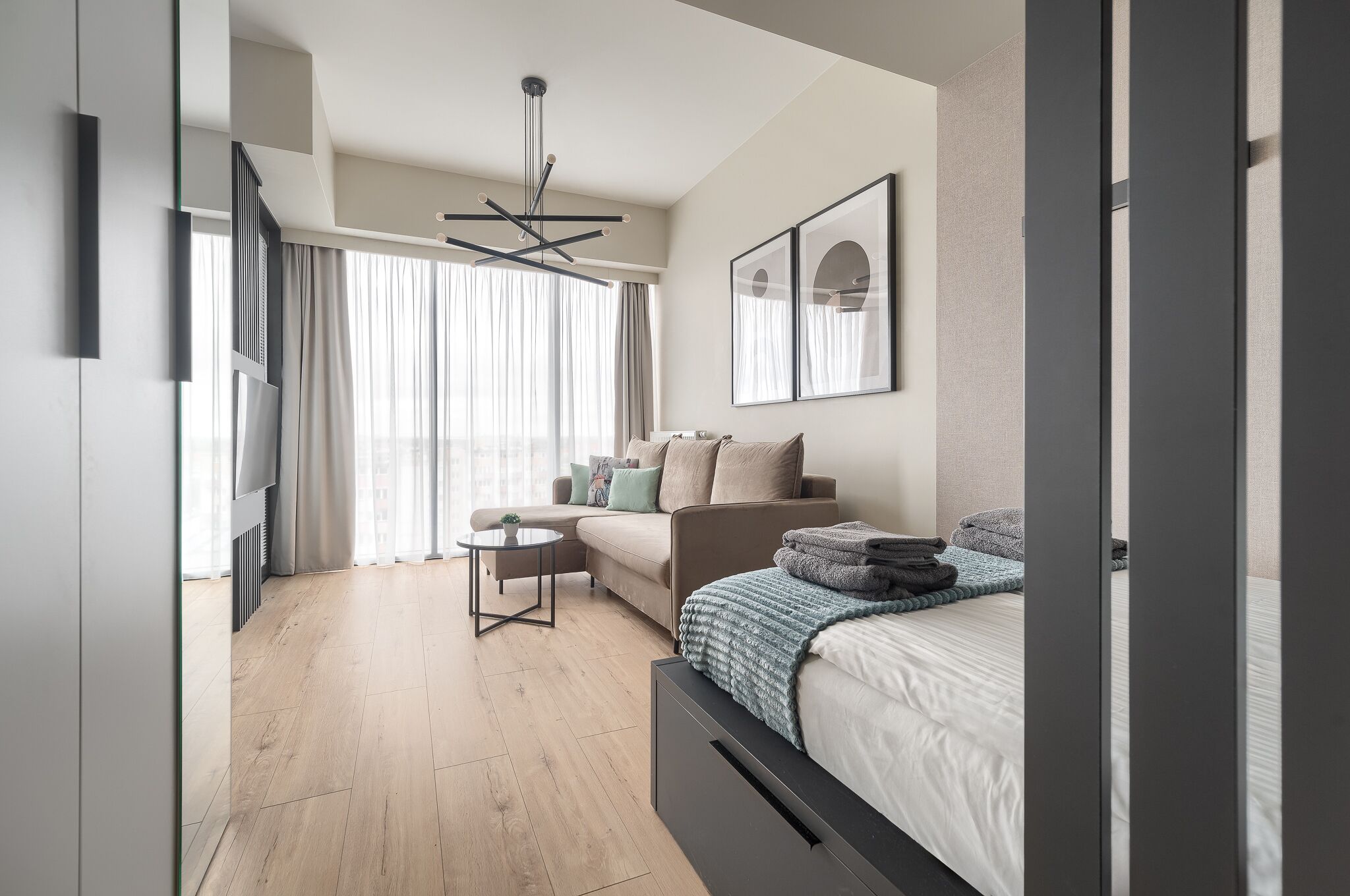Une chambre à coucher moderne avec un lit, un canapé, une petite table et une grande fenêtre avec des rideaux.
