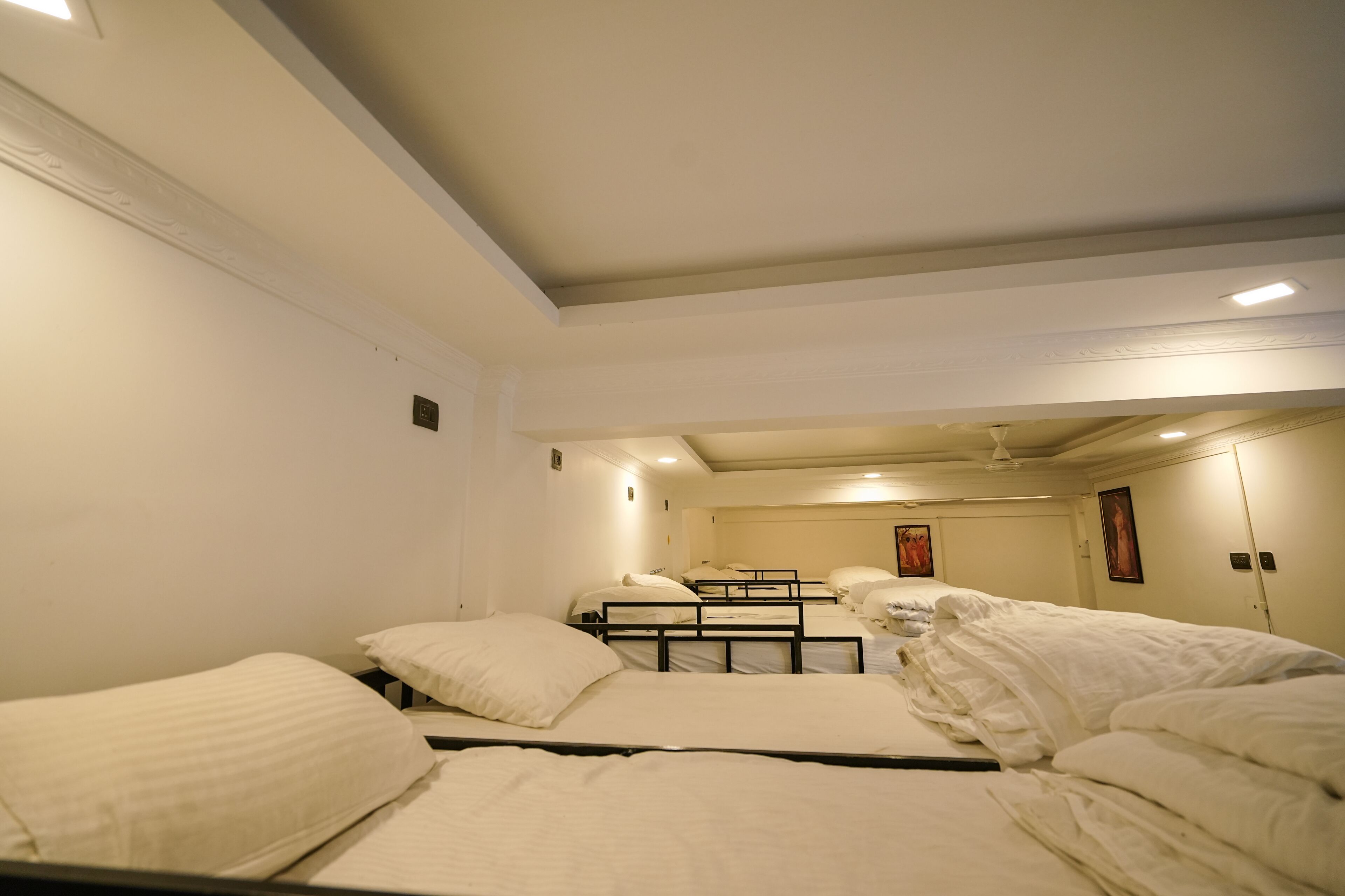 A hotel room with four single beds, a small table, and a ceiling fan.